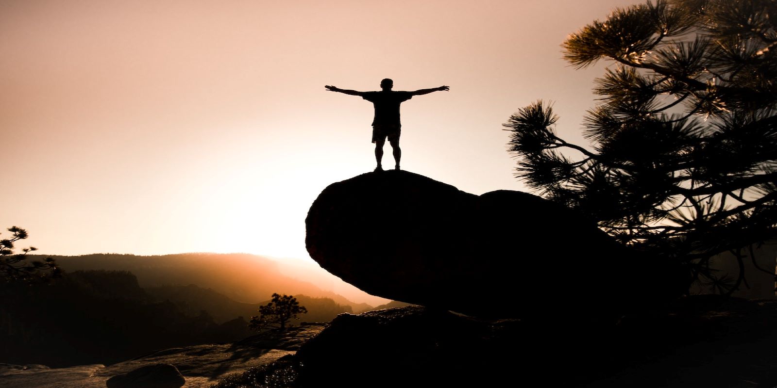 Inspirational Sunrise image of a hiker on a large rock